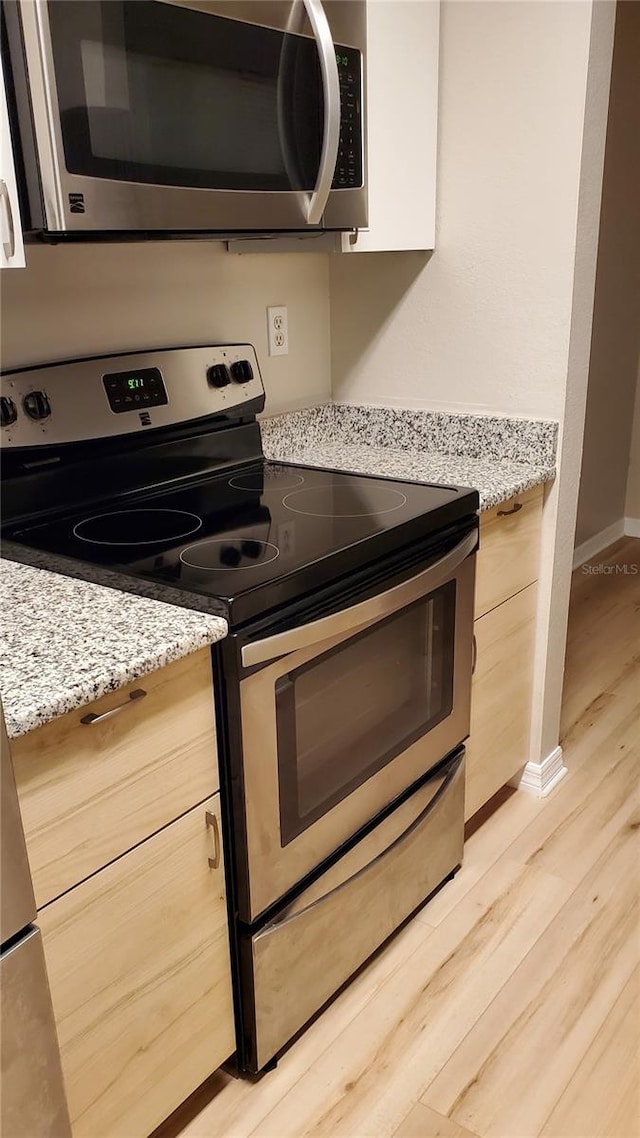 kitchen with baseboards, light stone countertops, stainless steel appliances, light wood-style floors, and light brown cabinets