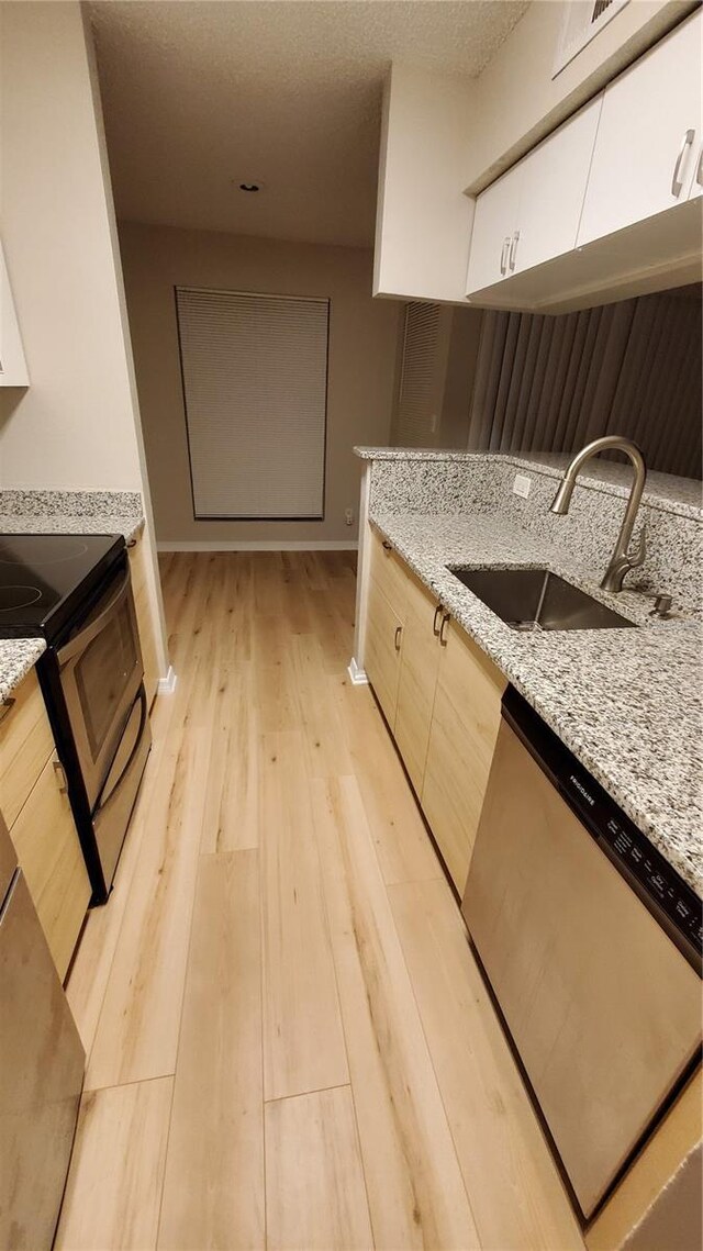 kitchen featuring light stone counters, light wood-style flooring, appliances with stainless steel finishes, white cabinetry, and a sink