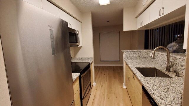 kitchen with light wood finished floors, stainless steel appliances, white cabinets, a sink, and light stone countertops