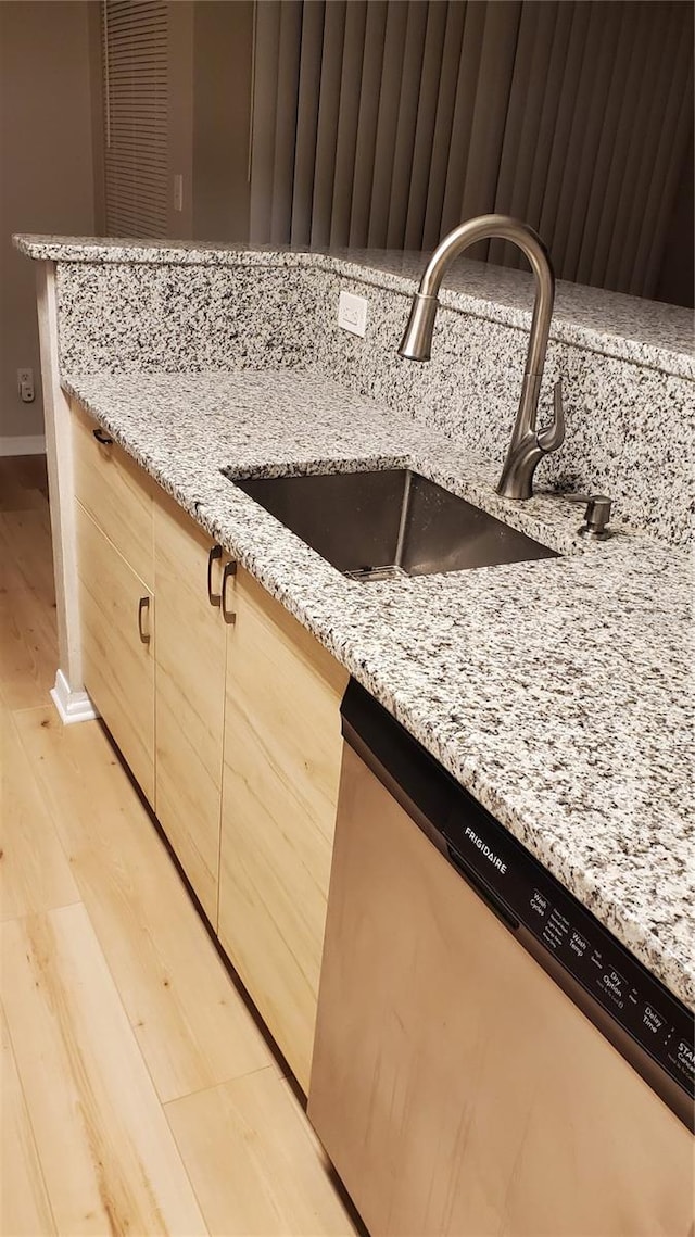 interior details with light stone counters, light brown cabinetry, light wood-type flooring, stainless steel dishwasher, and a sink