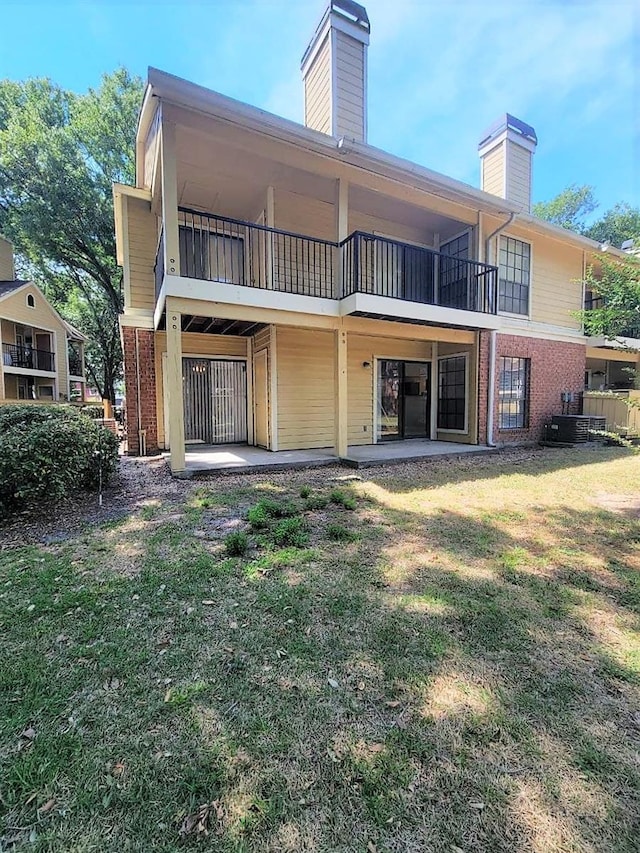 back of property with a yard, brick siding, a chimney, and a patio area