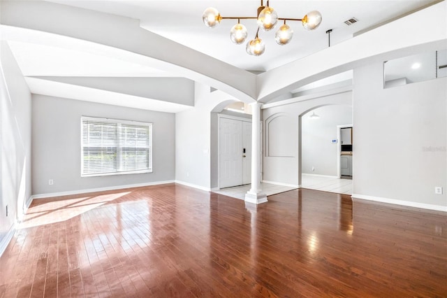 empty room with vaulted ceiling, a chandelier, decorative columns, and light hardwood / wood-style flooring