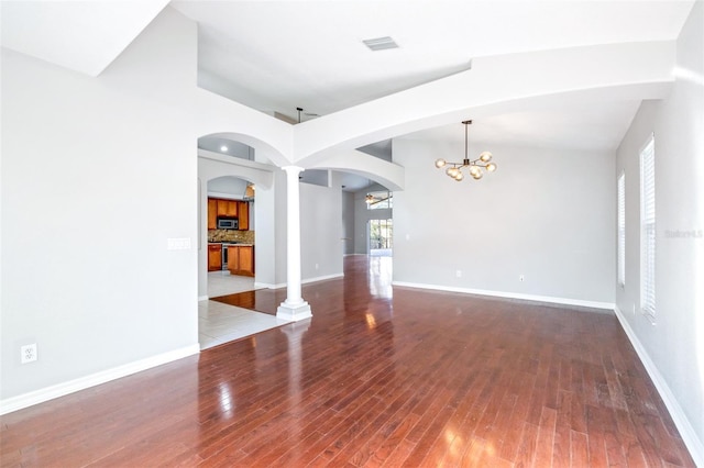 unfurnished room with wood-type flooring, a chandelier, and decorative columns