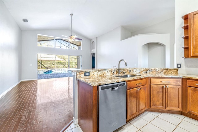 kitchen with lofted ceiling, sink, light stone counters, stainless steel dishwasher, and kitchen peninsula