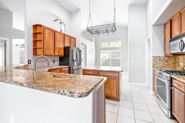 kitchen featuring appliances with stainless steel finishes, a high ceiling, light tile patterned floors, light stone counters, and kitchen peninsula