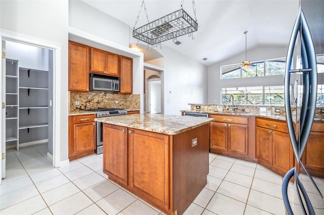 kitchen with sink, ceiling fan, appliances with stainless steel finishes, a center island, and light stone counters