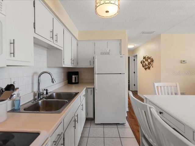 kitchen featuring light tile patterned flooring, sink, white cabinetry, tasteful backsplash, and white fridge