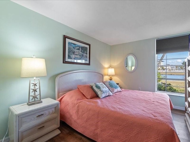 bedroom with a water view and dark hardwood / wood-style flooring