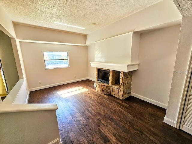 unfurnished living room featuring a textured ceiling, a fireplace, dark wood finished floors, and baseboards