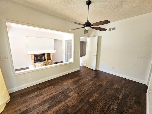 unfurnished living room with a fireplace, dark wood-type flooring, a textured ceiling, and ceiling fan