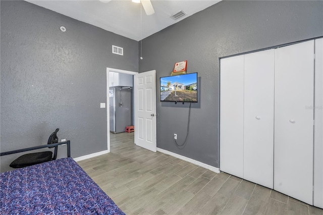 bedroom featuring stainless steel refrigerator, ceiling fan, light hardwood / wood-style floors, and a closet