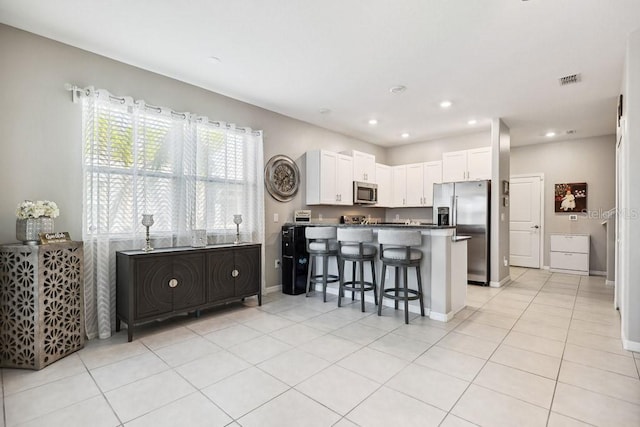 kitchen featuring appliances with stainless steel finishes, a breakfast bar, white cabinets, light tile patterned floors, and kitchen peninsula