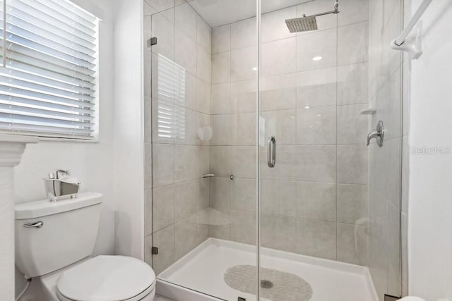 bathroom featuring a shower with door and toilet