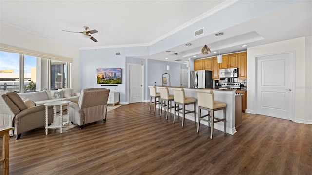 kitchen featuring a breakfast bar area, appliances with stainless steel finishes, dark hardwood / wood-style floors, ornamental molding, and a kitchen island