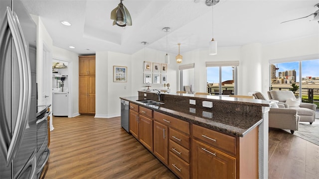 kitchen featuring decorative light fixtures, a center island with sink, dark stone counters, dark hardwood / wood-style floors, and stainless steel appliances