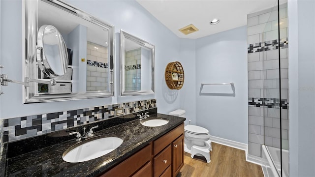 bathroom with backsplash, a tile shower, toilet, vanity, and hardwood / wood-style floors