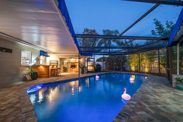 pool at dusk with a patio area, an outdoor bar, and glass enclosure