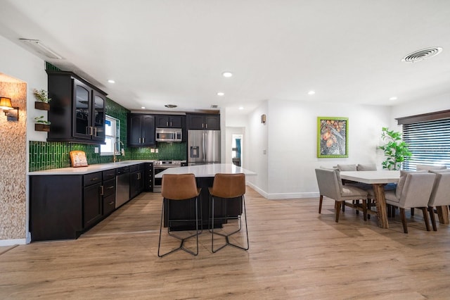 kitchen featuring sink, stainless steel appliances, a center island, tasteful backsplash, and light wood-type flooring