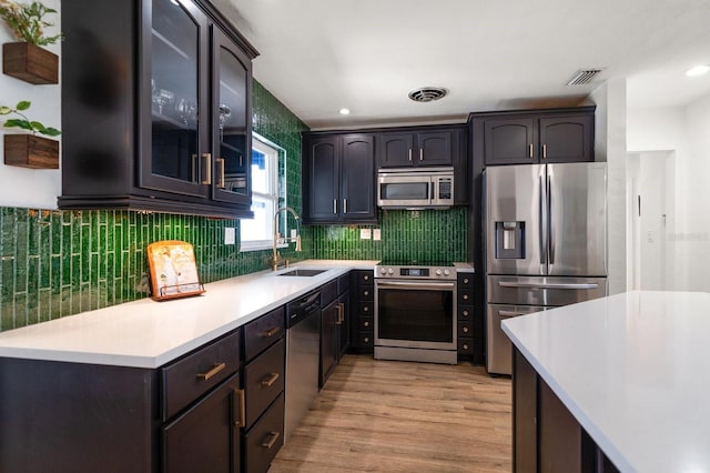 kitchen with dark brown cabinetry, sink, tasteful backsplash, light hardwood / wood-style flooring, and stainless steel appliances