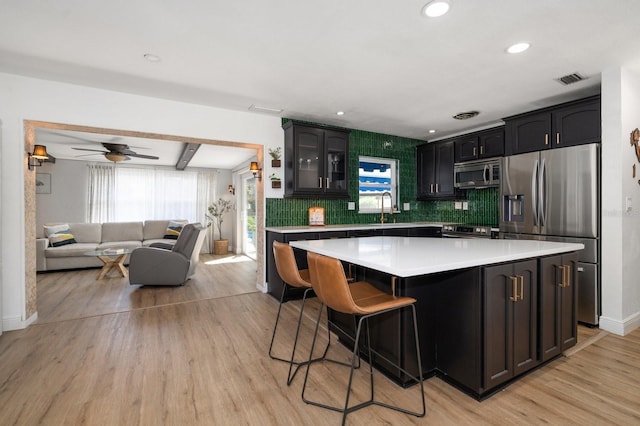 kitchen with decorative backsplash, stainless steel appliances, a kitchen island, and light hardwood / wood-style flooring