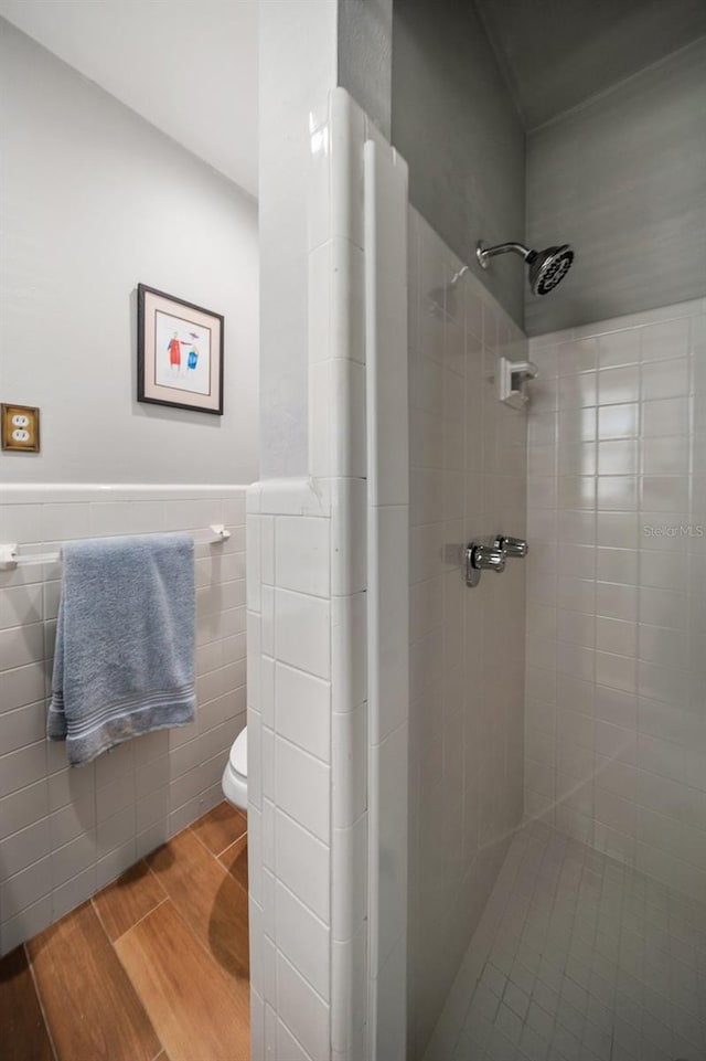 bathroom with tiled shower, toilet, hardwood / wood-style floors, and tile walls