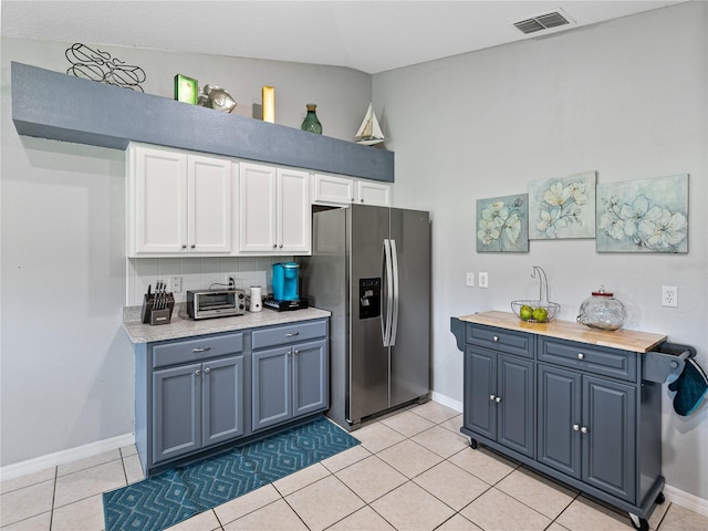 kitchen featuring light tile patterned floors, backsplash, blue cabinetry, stainless steel fridge with ice dispenser, and butcher block countertops