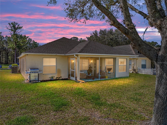 back house at dusk with central AC unit and a lawn