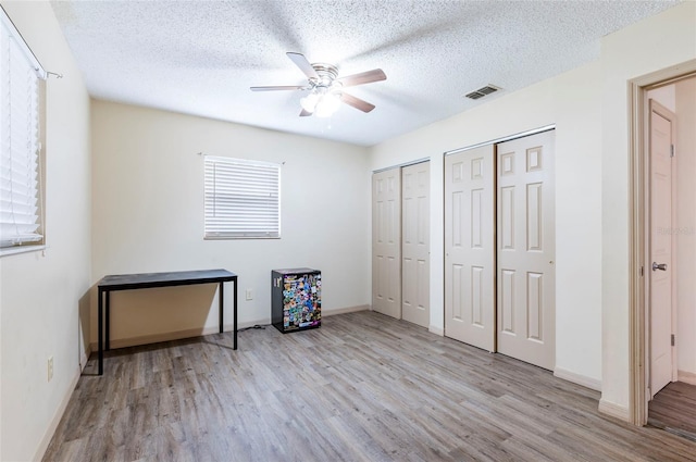 unfurnished bedroom with multiple closets, a textured ceiling, and light hardwood / wood-style flooring