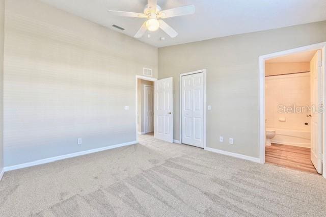 unfurnished bedroom featuring lofted ceiling, ensuite bath, light colored carpet, and ceiling fan