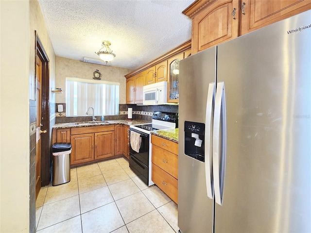 kitchen featuring sink, light tile patterned floors, range with electric stovetop, stainless steel fridge with ice dispenser, and dark stone counters