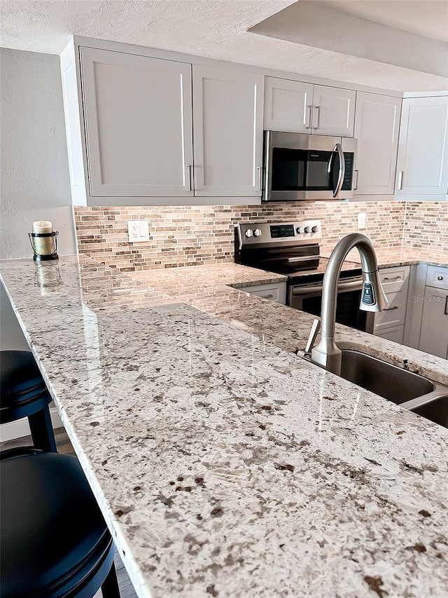 kitchen with sink, white cabinetry, light stone countertops, and stainless steel appliances