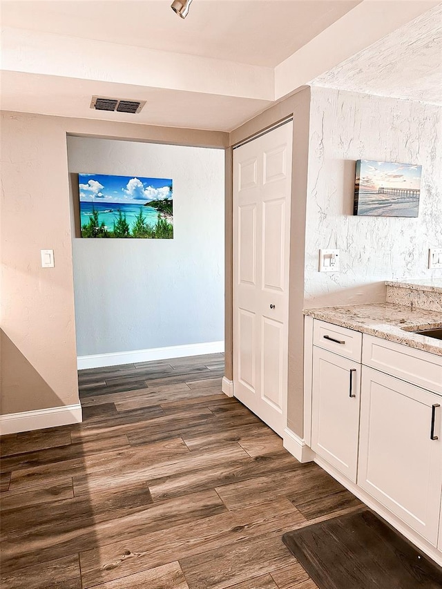 interior space with dark wood-type flooring, light stone countertops, and white cabinets