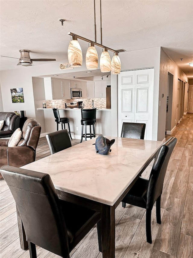 dining room featuring ceiling fan, a textured ceiling, and light hardwood / wood-style flooring