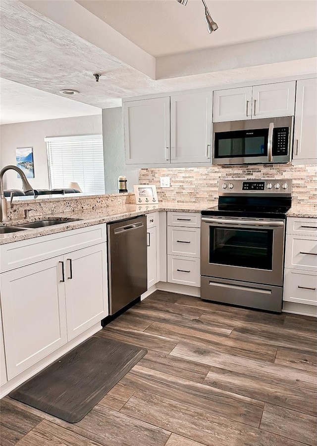 kitchen with appliances with stainless steel finishes, dark wood-type flooring, decorative backsplash, sink, and white cabinetry