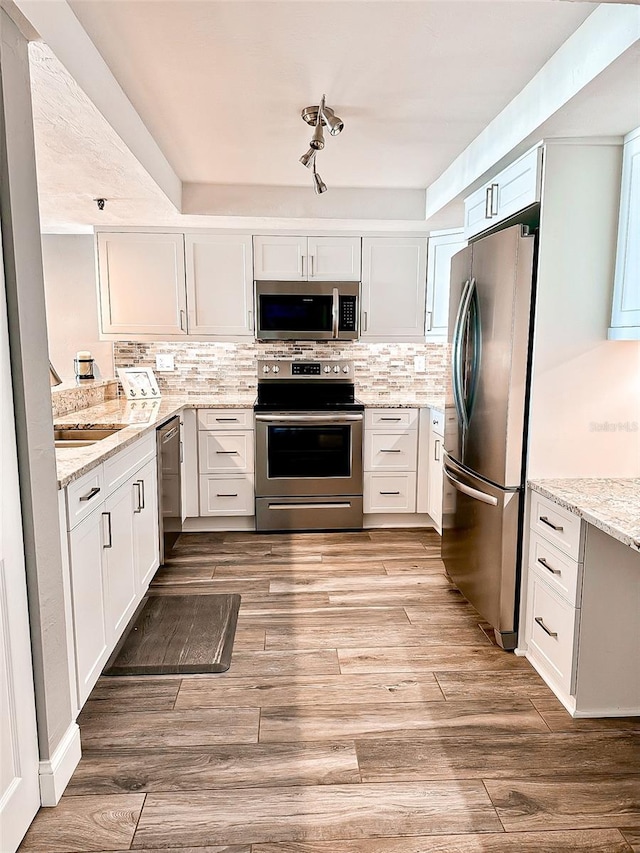 kitchen with light hardwood / wood-style flooring, appliances with stainless steel finishes, backsplash, white cabinetry, and light stone countertops