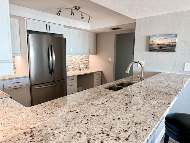 kitchen featuring kitchen peninsula, sink, white cabinetry, and stainless steel fridge