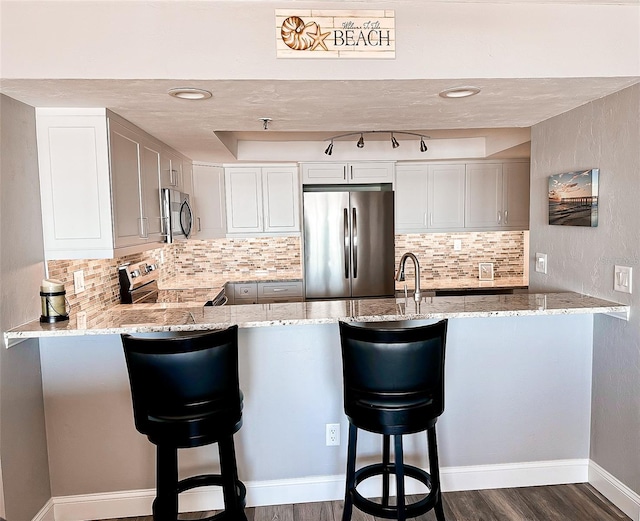 kitchen with appliances with stainless steel finishes, a breakfast bar, light stone counters, and kitchen peninsula