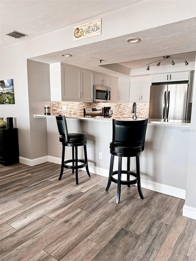 kitchen featuring appliances with stainless steel finishes, wood-type flooring, white cabinets, a kitchen bar, and kitchen peninsula