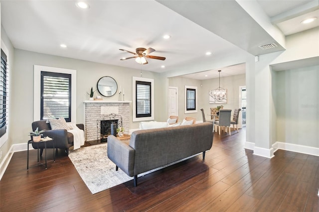 living room with plenty of natural light, ceiling fan with notable chandelier, a fireplace, and dark hardwood / wood-style flooring