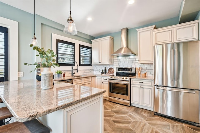 kitchen featuring sink, a kitchen breakfast bar, hanging light fixtures, stainless steel appliances, and wall chimney exhaust hood