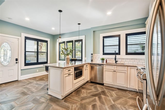 kitchen featuring sink, hanging light fixtures, stainless steel appliances, light stone countertops, and cream cabinets