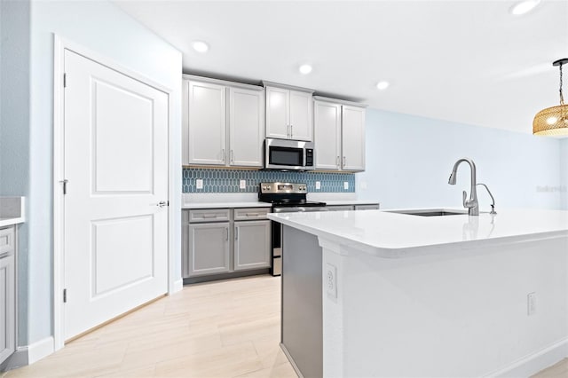 kitchen featuring pendant lighting, sink, gray cabinetry, a kitchen island with sink, and stainless steel appliances