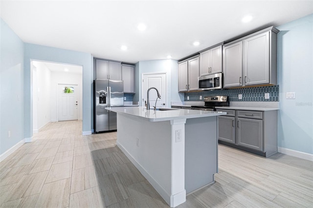 kitchen featuring sink, gray cabinetry, tasteful backsplash, a center island with sink, and stainless steel appliances