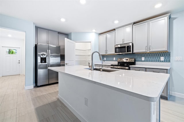 kitchen with sink, light stone counters, appliances with stainless steel finishes, a kitchen island with sink, and decorative backsplash