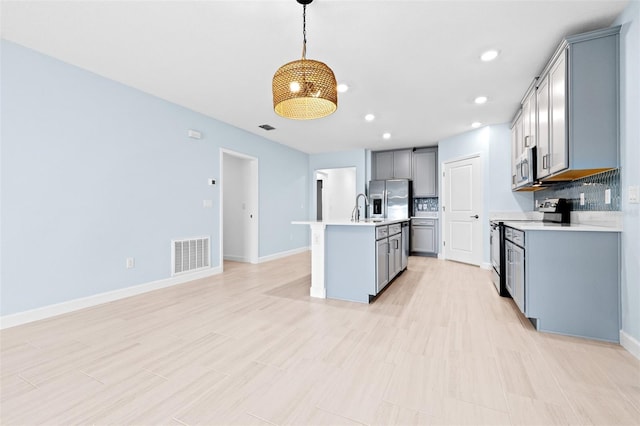 kitchen with decorative light fixtures, tasteful backsplash, sink, stainless steel appliances, and a center island with sink