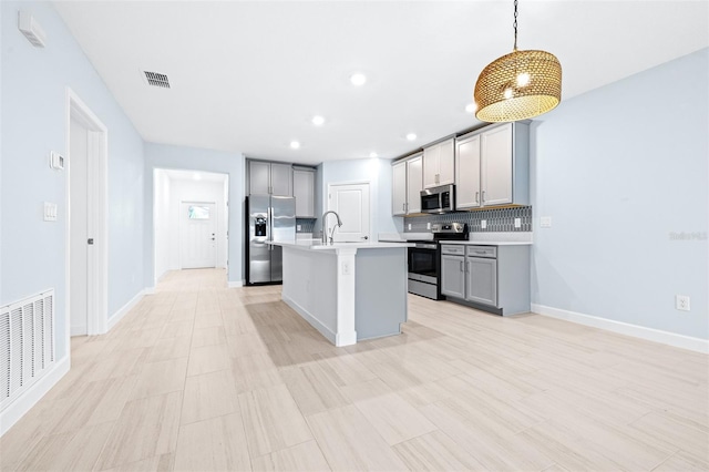 kitchen with gray cabinets, a kitchen island with sink, hanging light fixtures, stainless steel appliances, and decorative backsplash