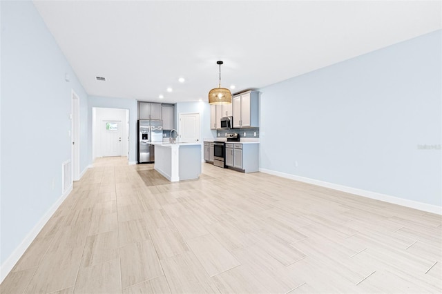 kitchen featuring gray cabinetry, hanging light fixtures, stainless steel appliances, a center island with sink, and light hardwood / wood-style flooring