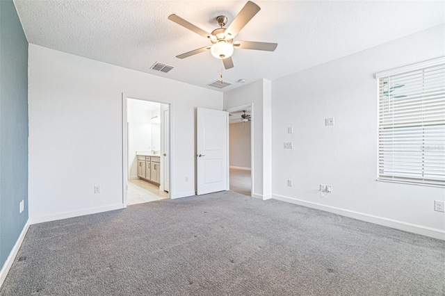 unfurnished bedroom with ceiling fan, light colored carpet, a textured ceiling, and ensuite bathroom