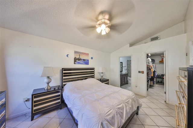 bedroom featuring vaulted ceiling, a walk in closet, light tile patterned floors, a textured ceiling, and a closet