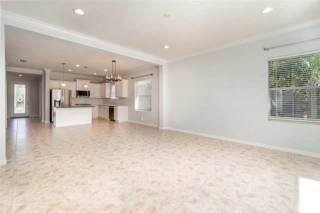 unfurnished living room with sink, plenty of natural light, ornamental molding, and a chandelier